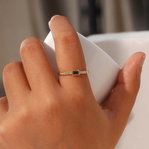 "Close-up of a ring with a rectangular onyx stone set on a thin band encrusted with cubic zirconia, combining elegance and sophistication."